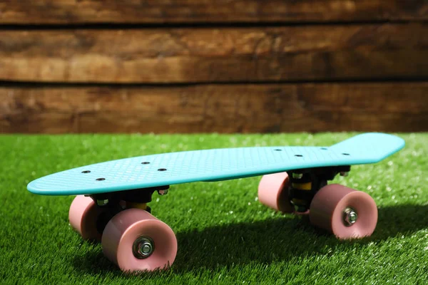 Světle Modrý Skateboard Růžovými Koly Zelené Trávě Blízkosti Dřevěné Zdi — Stock fotografie