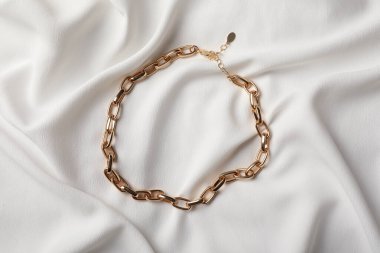 Beyaz kumaş üzerinde zarif altın kolye, üst manzara. Şık bijouterie