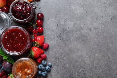 Farklı reçelli kavanozlar ve gri masada taze meyveler. Metin için boşluk
