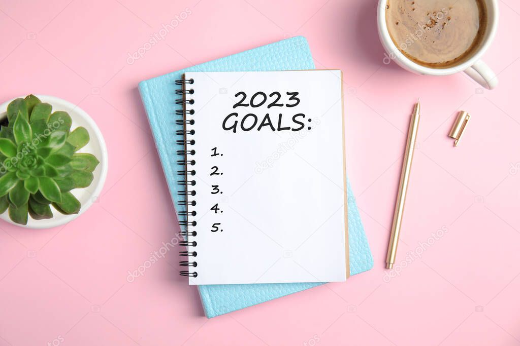 Notebook with inscription 2023 Goals, cup of coffee, plant and pen on pink background, flat lay. New Year aims 