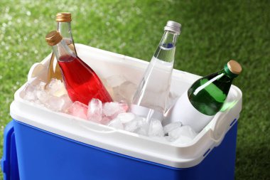 Mavi plastik kutu. İçecekler ve yeşil çimenlerin üzerinde buz küpleri.