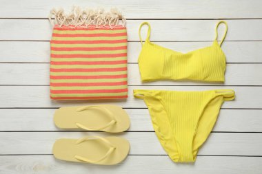 Plaj havlusu, mayo ve terlikler beyaz ahşap arka planda, düz yatıyordu.