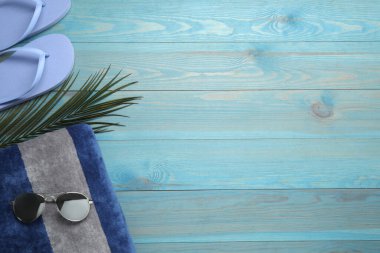 Plaj havlusu, parmak arası terlik ve açık mavi ahşap arka planda güneş gözlüğü. Metin için boşluk