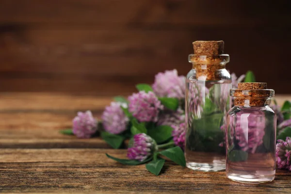 Beautiful clover flowers and bottles of essential oil on wooden table, closeup. Space for text