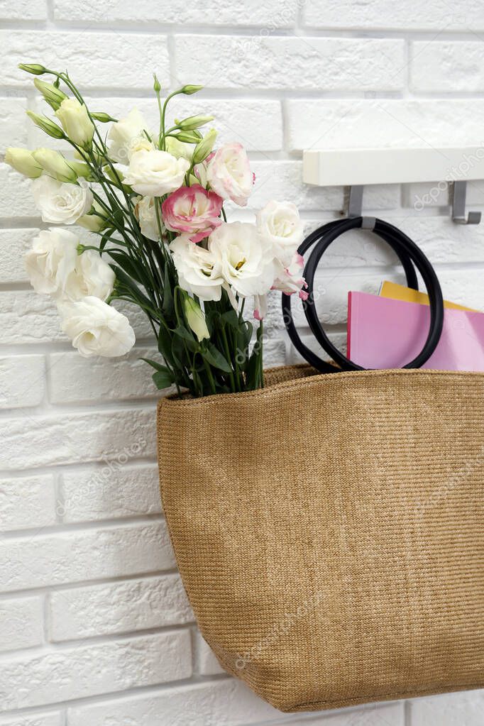 Stylish beach bag with beautiful bouquet and magazines hanging on hook rack indoors
