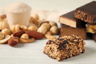 Farklı lezzetli protein çubukları ve fındıklar beyaz masada, yakın plan.