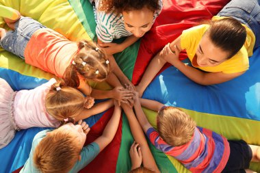 Gökkuşağı paraşütünde el ele tutuşan öğretmenleri olan bir grup çocuk. Yaz kampı aktivitesi