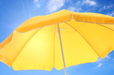 Büyük sarı plaj şemsiyesi ve arkasında beyaz bulutlar olan güzel mavi gökyüzü.
