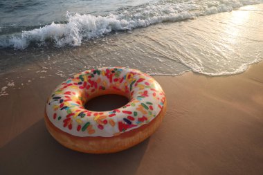 Deniz kenarındaki kumlu kumsalda donut desenli şişirilebilir halka, metin için boşluk.