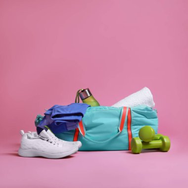 Pembe arka planda mavi spor çantası ve spor aksesuarları.