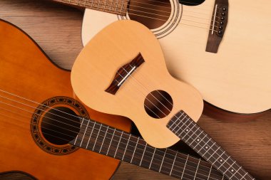 Tahta arka planda Ukulele ve akustik gitarlar, düz yatış. Dizgi müzik aletleri