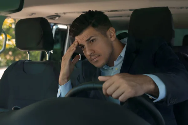 Stressed man in driver\'s seat of modern car, view through windshield