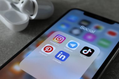 MYKOLAIV, UKRAINE - 10 Ağustos 2021: Apple iPhone X, Airpod 'lar ve gri masada şarj çantası. Farklı sosyal medya simgelerine sahip ekran, kapat