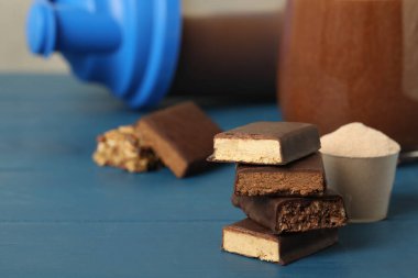 Farklı enerji çubukları, protein kokteyli ve mavi ahşap masada toz. Metin için boşluk