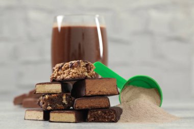 Farklı enerji çubukları, protein kokteyli ve gri masadaki toz.