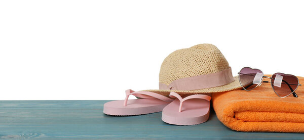 Beach towel, flip flops, straw hat and heart shaped sunglasses on light blue wooden surface against white background. Space for text