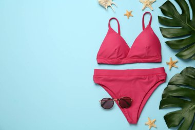 Açık mavi arka planda şık bikini ve plaj aksesuarları, düz yatış. Metin için boşluk