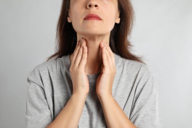 Mature woman doing thyroid self examination on light background, closeup clipart