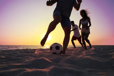 Arkadaşlar gün batımında plajda futbol oynuyor, yakın plan.