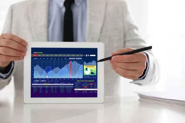 Man analyzing electronic trading platform on tablet indoors, closeup. Stock exchange