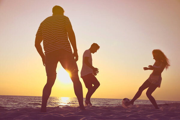 Friends playing football on beach at sunset