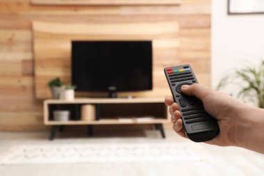 Genç adam TV 'de uzaktan kumandayla kanal değiştiriyor.