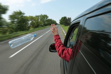 Driver throwing away plastic bottle from car window. Garbage on road clipart