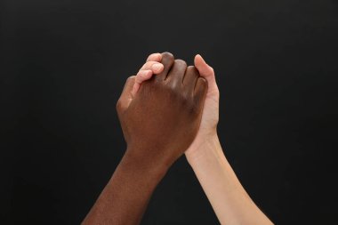 Kadın ve Afrikalı Amerikalı erkek siyah arkaplanda el ele tutuşuyor.