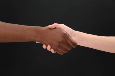 Kadın ve Afrikalı Amerikalı erkek siyah arka planda el sıkışıyor, yakın plan.