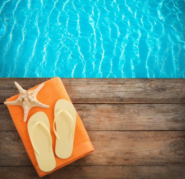 Plaj havlusu. Yüzme havuzunun yanındaki ahşap yüzeyde parmak arası terlikler ve deniz yıldızları. Metin için boşluk 