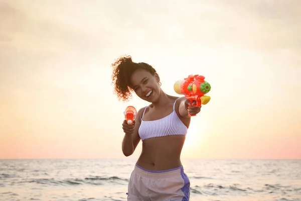日没時にビーチで楽しい水銃を持つアフリカ系アメリカ人女性 — ストック写真