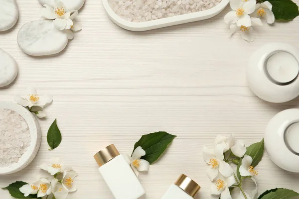 Frame of beautiful jasmine flowers, spa stones and skin care products on white wooden table, flat lay. Space for text