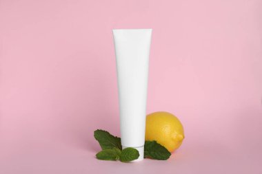 Boş diş macunu tüpü, pembe arka planda taze nane ve limon.