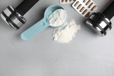 Açık gri masada bir kepçe amino asit tozu, haplar ve dambıllar düzleştiriliyor. Metin için boşluk