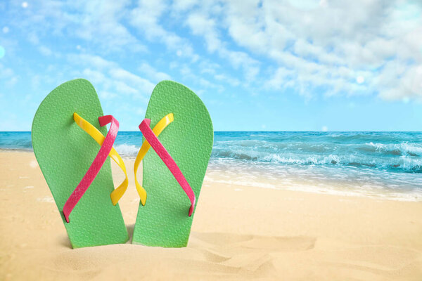 Green flip flops on sandy beach near sea. Space for text 
