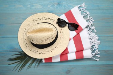 Plaj havlusu, güneş gözlüğü ve açık mavi ahşap arka planda hasır şapka.