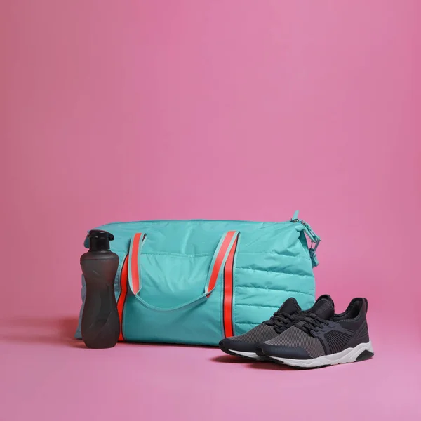 Blue gym bag and sports accessories on pink background