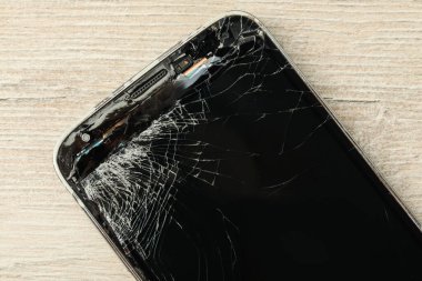 Açık bej ahşap arka planda çatlak ekranlı akıllı telefonun üst görüntüsü, yakın plan. Aygıt onarımı