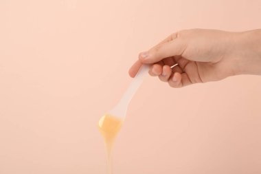 Bej arka planda sıcak tüy dökücü balmumu olan spatula tutan kadın, yakın plan. Metin için boşluk