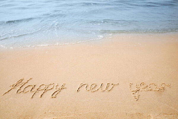 Sandy beach with text Happy New Year washed by sea