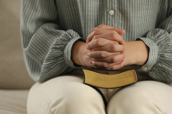 Religious woman praying over Bible on sofa, closeup