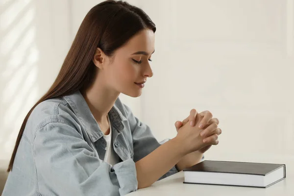 屋内のテーブルで聖書を祈る宗教的な若い女性 — ストック写真