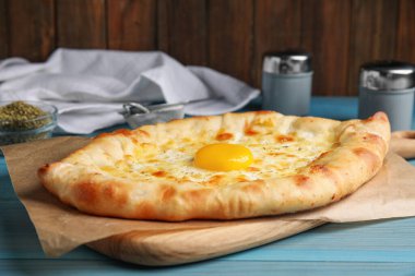 Açık mavi ahşap masada peynirli ve yumurtalı taze ev yapımı khachapuri.