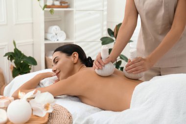 Genç bir kadın kaplıca salonunda bitkisel masaj yaptırıyor.