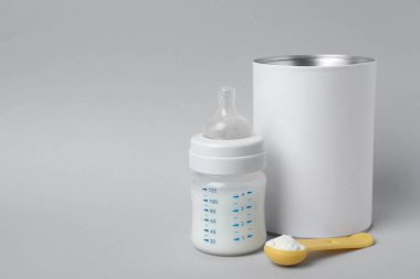 Açık gri arka planda bir kepçe dolusu toz bebek maması ve beslenme şişesi, mesaj için boşluk. Bebek sütü