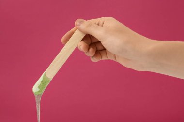 Fuşya arka planında sıcak tüy döken bir spatula tutan kadın, yakın plan.