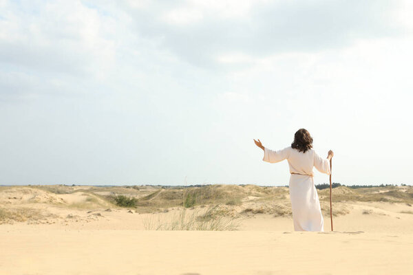 Jesus Christ raising hand in desert, back view. Space for text