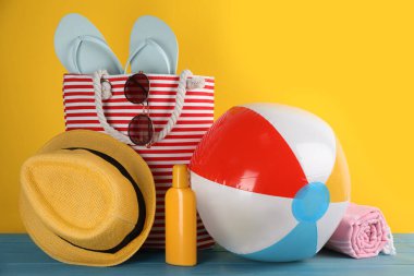 Renkli şişme top ve farklı plaj aksesuarları açık mavi ahşap masa üzerinde sarı arka plan