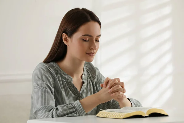 屋内のテーブルで聖書を祈る宗教的な若い女性 — ストック写真