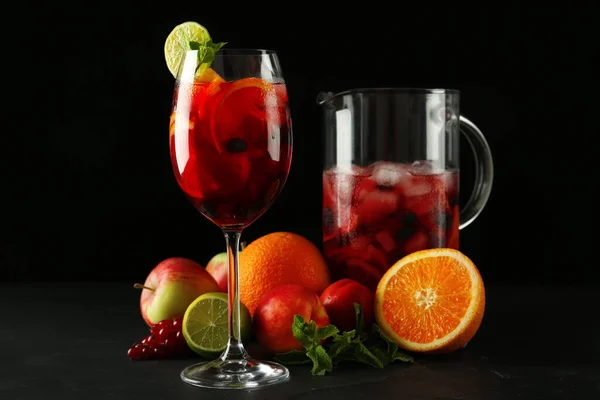 Glass and jug of Red Sangria with fruits on black table